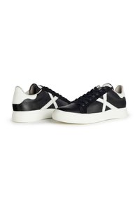 Sneaker in pelle nera con accenti bianchi, superficie testurizzata, punta arrotondata, suola piatta in gomma bianca e design con lacci. Modello distintivo ai lati.