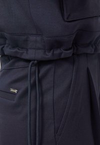 Nahaufnahme von dunkelblauen Sweatpants mit elastischem Bund, Kordelzug, Seitentasche und kleinem metallischem Markenschild.