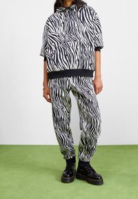 Sudadera y joggers de estampado de cebra en blanco y negro, con capucha y puños acanalados. Combinados con botas negras de cordones sobre un suelo verde.