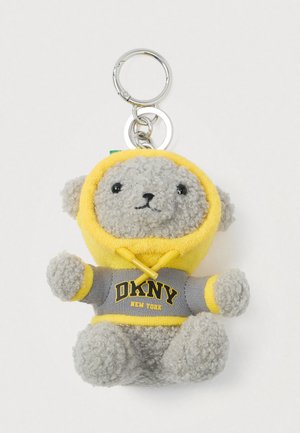 Šedý plyšový medvídek na klíče v žluté mikině s kapucí, na které je nápis "DKNY New York" v černém a žlutém písmu.