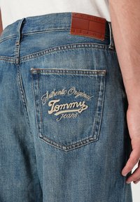 Plave traperice s stražnjim džepom na kojem je izvezeni tekst "Authentic Original Tommy Jeans" i smeškanim kožnim logom.