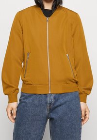 Musztardowa kurtka bomberka z zamkiem z przodu, ściągaczami na mankietach i dwoma bocznymi kieszeniami na zamek; gładka faktura i dopasowany krój.