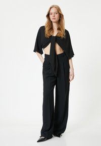 Sort cropped top med knyt foran, parret med højtaljede sorte vide bukser. Tilbehøret inkluderer elegante sorte sko.
