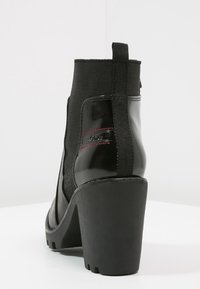Bottes noires à la cheville avec une tige en cuir verni et textile, un haut talon bloc, un panneau élastique et des coutures d'accent rouge.