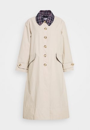 Long manteau beige avec de gros boutons, des poches à rabat, des pattes aux poignets et un col à carreaux foncés, sur un fond uni.