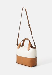 Sac en cuir avec une partie supérieure crème et une partie inférieure marron. Il dispose de double poignées et d'une bandoulière ajustable.