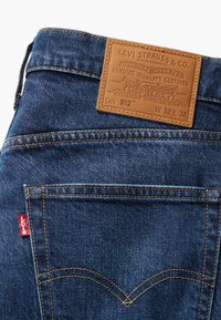 Modre kavbojke z zadnjim žepom, ki ima bež usnjeno oznako Levi Strauss & Co. in rdečo tkaninsko oznako Levi's na stranskem šivu, velikost W32 L32.