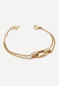 Gold bracelet featuring two linked chains, one adorned with clear gemstones. Includes a triangular tag with the brand name, clasp closure.