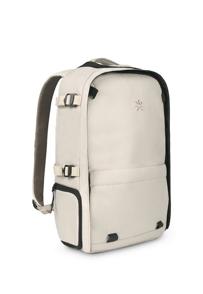 Mochila beige con una superficie texturizada, correas ajustables, bolsillos laterales y acentos negros. Cuenta con un hardware resistente y una marca mínima.