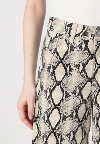 Pantalones de imitación de serpiente en beige y negro, con un diseño de cintura alta, bolsillos frontales y un acabado texturizado.