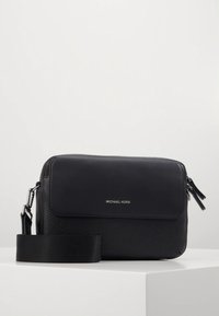 Musta nahkainen olkalaukku, jossa on teksturoitu pinta, tasainen etutasku, hopeiset metalliosat ja säädettävä hihna. Michael Korsin logo näkyvissä.