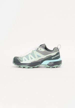 Lichtblauwe en grijze Salomon trailrunningschoen met robuuste zool en witte veters, zijaanzicht op witte achtergrond.