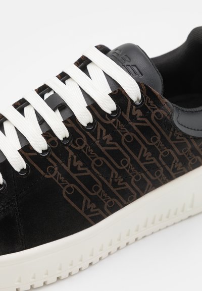 Sneakers in suede nera con un motivo logo marrone, lacci bianchi e suola in gomma bianca testurizzata. Accenti in pelle nera sul tallone.
