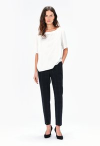 Blusa bianca a maniche corte con scollatura ampia, abbinata a pantaloni slim-fit a quadri blu navy. Indossata con scarpe col tacco nere.