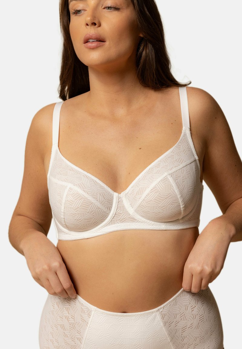 Soutien-gorge en tissu blanc avec motif géométrique, design avec armatures, bretelles réglables et texture semblable à de la dentelle, porté avec des culottes taille haute assorties.