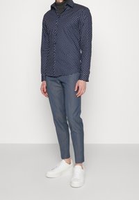 Marinblus med vitt geometriskt mönster, knäppbar krage, långa ärmar, ihop med grå slim-fit byxor och vita sneakers.