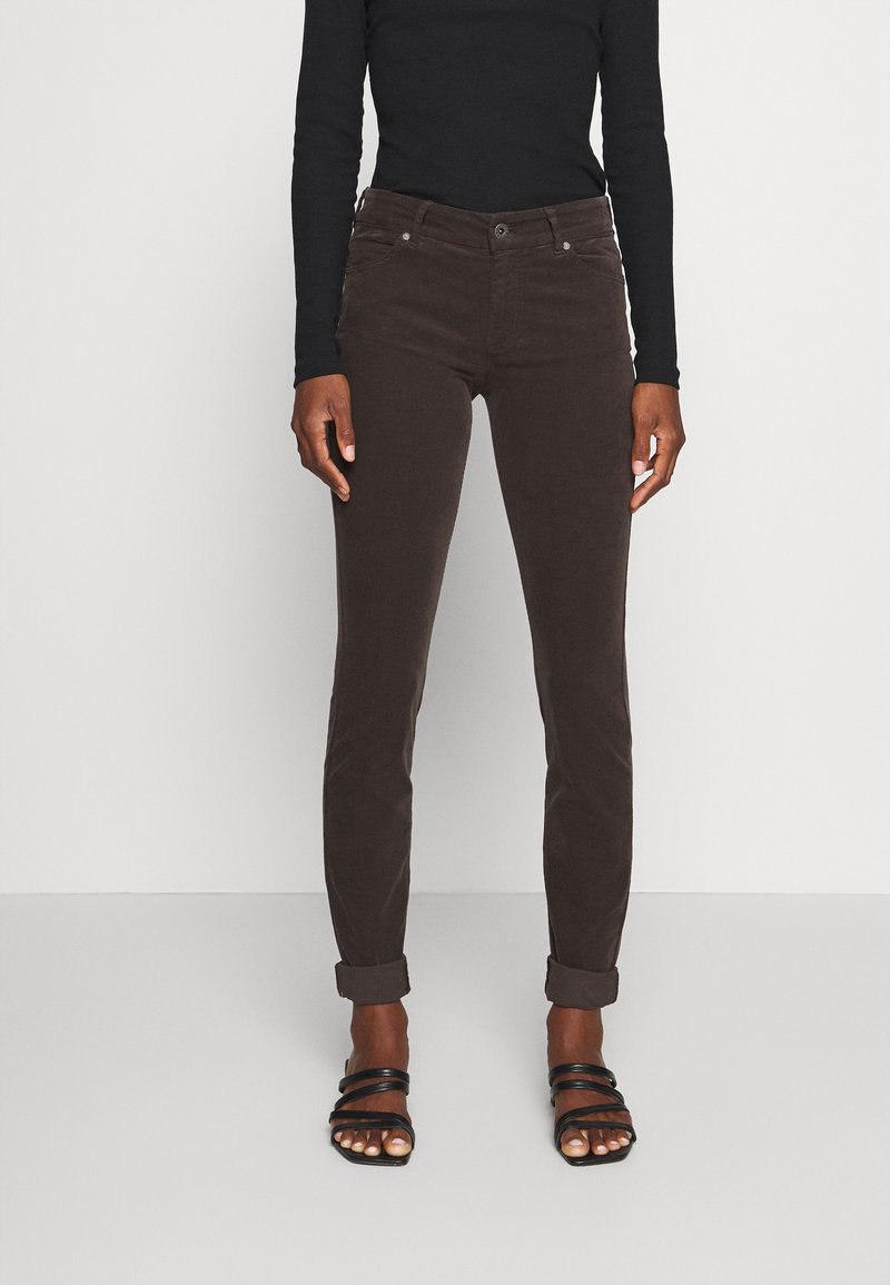Bruine corduroybroek met een slim fit, voorzien van een knoopsluiting, vijf zakken en opgerolde broekspijpen. Gecombineerd met zwarte sandaaltjes met bandjes.