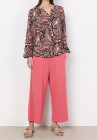 Blouse à manches longues avec un motif cachemire en nuances de rose, marron et vert ; associée à un pantalon ample rose et des sandales à talons beiges.