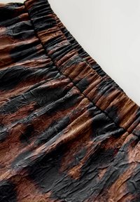 Elastische taillebandstof met een gekreukt textuur in een donkerbruin en zwart tie-dye patroon op een licht achtergrond.