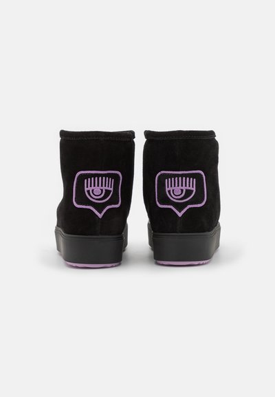 Botas de tobillo de ante negro con un gráfico de ojo púrpura y un diseño de bocadillo en la parte trasera. Presenta una suela de goma negra.