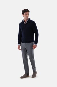 Marineblauer Sweater mit Reißverschluss, graue maßgeschneiderte Hose und graue Stiefel. Der Sweater hat gerippte Bündchen und einen Saum und ist über ein kariertes Hemd geschichtet.