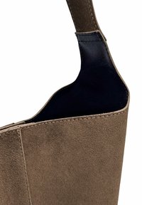 Sac à main en daim marron avec un extérieur texturé, un intérieur en cuir lisse et une forme minimaliste. Il possède une seule poignée robuste.