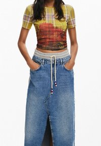 Krátký rukáv žlutý kostkovaný crop top s přírodním potiskem, spárovaný s modrou džínovou sukní s vysokým pasem, která má stahovací šňůrku a postranní rozparek.