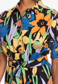 Blommig kortärmad klänning med livfulla färger: svart bakgrund med orange, blå och gula blommor, knappar framtill och midjeband.