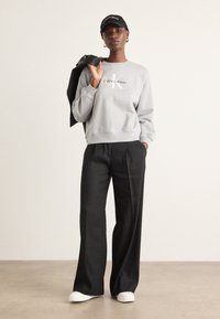 Gray sweatshirt with "Calvin Klein" logo, black wide-leg trousers, white sneakers, and a black cap, with a leather jacket draped over the shoulder.