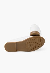 Scarpe bianche con materiale superiore liscio, caratterizzate da una punta rotonda e una suola in gomma bassa di colore tan con un motivo di grip texturizzato.
