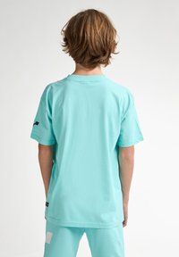 Camiseta de algodón verde menta con mangas cortas, cuello redondo y costuras planas. Presenta un pequeño logo negro en la manga izquierda.
