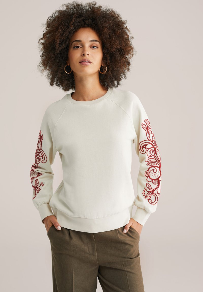 Felpa color crema con maniche lunghe, caratterizzata da intricate ricami floreali rossi su entrambe le maniche; vestibilità morbida e polsini a coste.