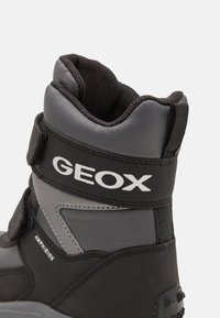 Čierne a sivé čižmy s textúrovaným zvrškom, suchým zipsom a výrazným logom GEOX. Navrhnuté pre odolnosť a vodoodolnosť.