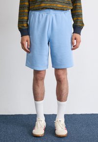 Lyseblå joggebukser med elastisk midje og sidelommer, laget av mykt materiale. Kombinert med hvite sokker og kremfargede sneakers.