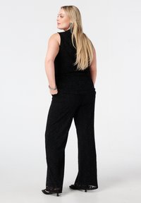 Zwart kanten tweedelig outfit met een mouwloze top en wijd uitlopende broek met een bloemenpatroon en doorschijnende kanten afwerking aan de zoom.