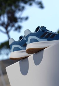 Scarpe sportive blu con tomaia in mesh strutturato, intersuola bianca e suola in gomma color marrone chiaro, con dettagli neri e una fascetta di sicurezza.