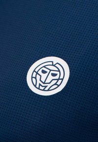 Tejido texturizado en azul marino con un emblema blanco redondo que presenta un diseño de cara estilizada en líneas azul oscuro.