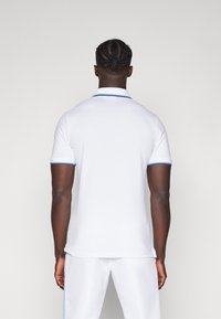 Polo shirt bianco a maniche corte, con una finitura blu lungo il colletto e i bordi delle maniche. Tessuto liscio, taglio classico.