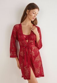 Czerwony szlafrok w stylu kimona z rękawami 3/4, kwiatowymi wzorami, głębokim dekoltem w kształcie litery V oraz satynowym paskiem wiązanym w talii. Przezroczysta tekstura.