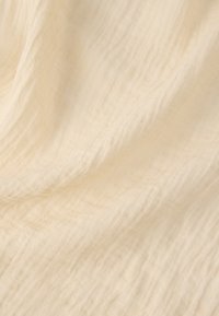 Zachte, roomkleurige stof met subtiele verticale en horizontale kreukels die een zacht, gestructureerd patroon vormen.