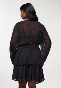 Czarna sukienka warstwowa z przezroczystą, teksturowaną warstwą, z długimi rękawami i elastycznym pasem, oferująca luźny krój i warstwowy design.