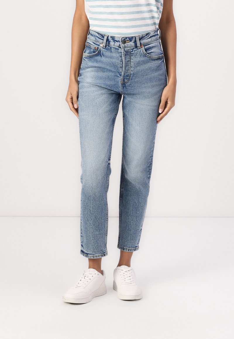 Jeans de tiro alto azul claro con pierna recta, que presentan un desgaste sutil, cinco bolsillos y un dobladillo recortado, combinados con zapatillas blancas.