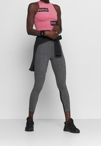 Crop top sportivo rosa Nike con marchio nero, abbinato a leggings grigi a vita alta con una striscia laterale nera. Scarpe sportive nere.