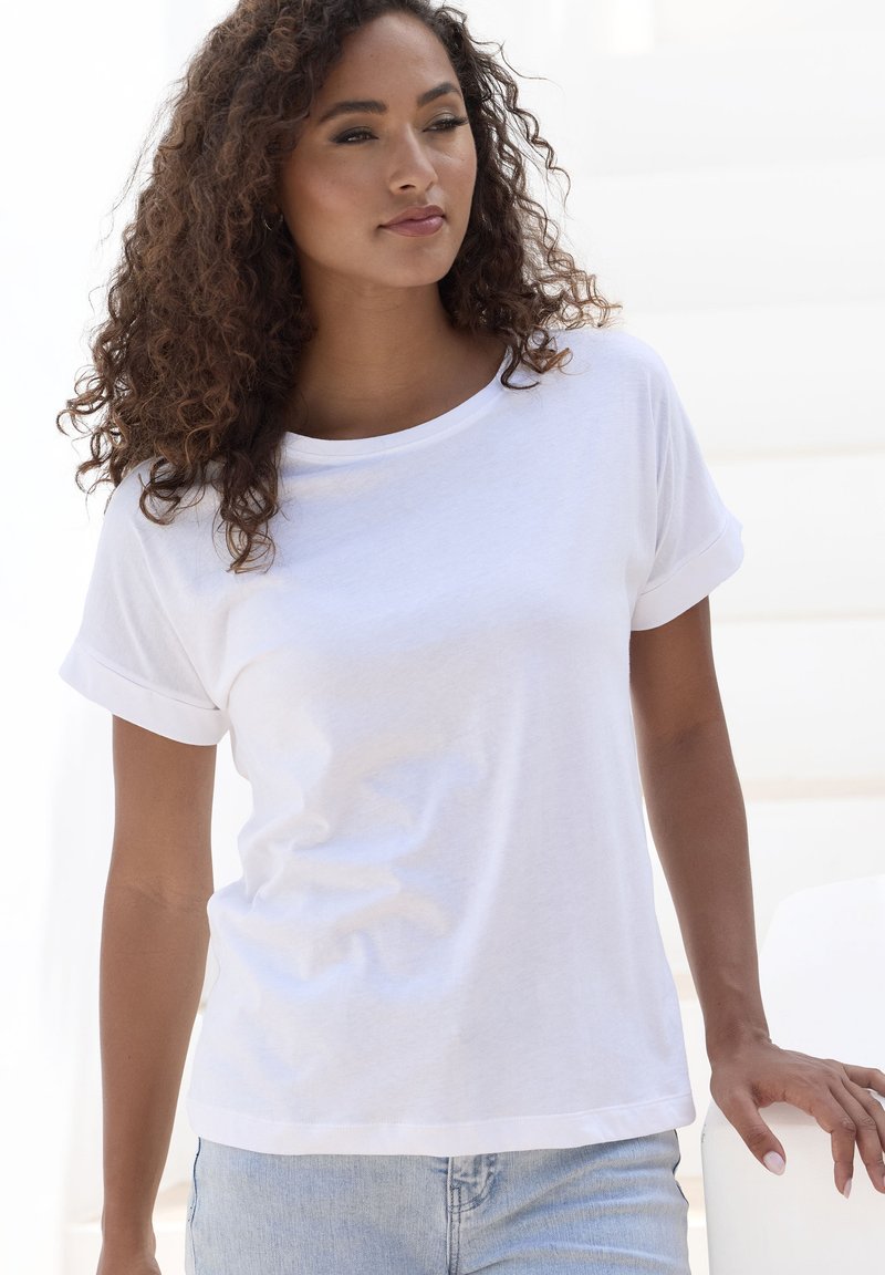 Weißes Baumwoll-T-Shirt mit lässigem Schnitt und umgeschlagenen kurzen Ärmeln, kombiniert mit hellblauen Jeans. Glatte Textur, minimalistisches Design.