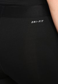 Leggings Dri-Fit neri caratterizzati da una texture liscia e un design aderente. La vita presenta un logo stampato in bianco.