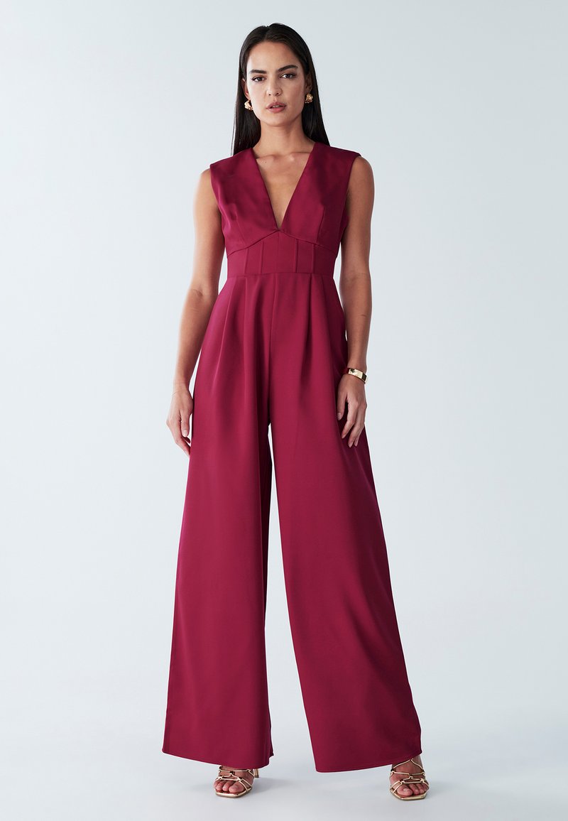 Burgundy jumpsuit med djup V-ringning, vida ben och texturerad bodice. Tillverkad av slätt tyg, med figursydd midja och veck.