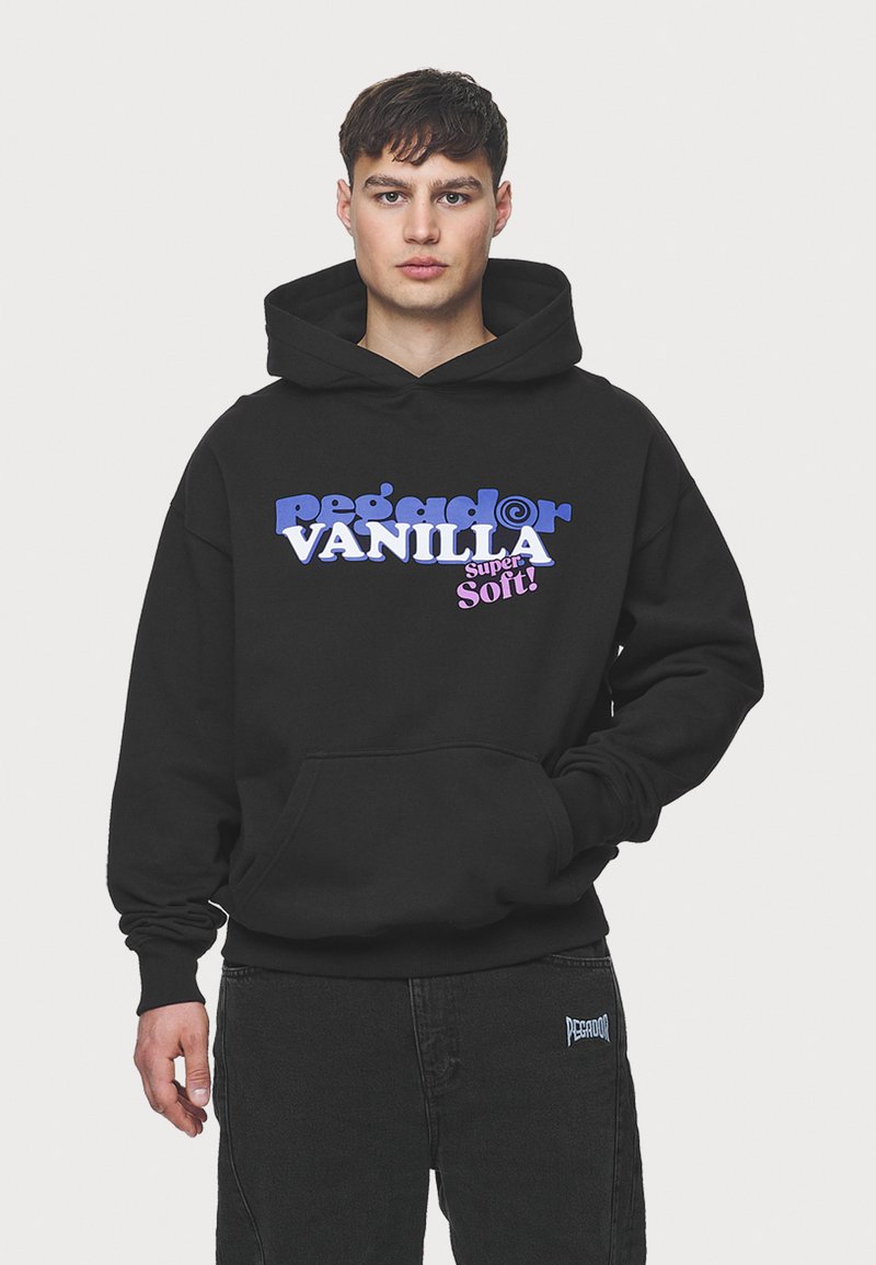 Črn hoodie s sprednjim žepom, ki vsebuje drzne napis v vijolični in roza barvi "pega dor VANILLA super Soft!" na gladki teksturi blaga.