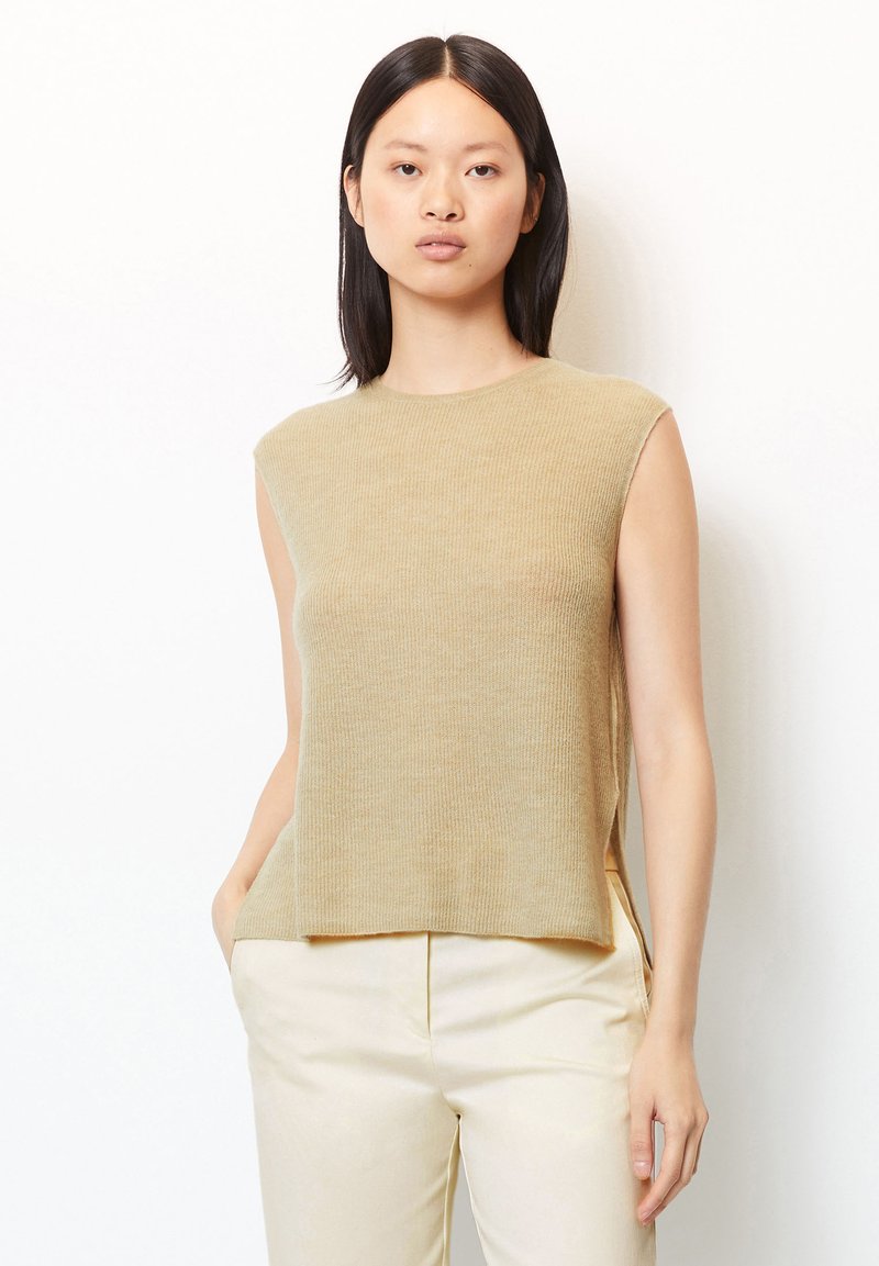 Beige ärmelloses Strickoberteil mit strukturierter Oberfläche, Rundhalsausschnitt und seitlichen Schlitzen, kombiniert mit cremefarbenen Hosen.