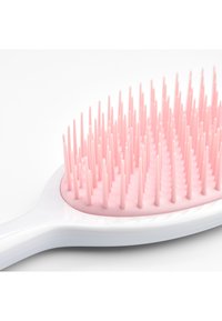 Brosse à cheveux blanche avec un manche incurvé et des poils roses doux et flexibles disposés en rangées sur la tête de la brosse.