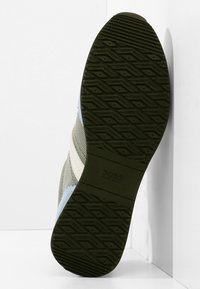 Semelle d'une chaussure noire en caoutchouc avec un motif géométrique et un marquage "BOSS HUGO BOSS", associée à une tige en tissu bleu clair et beige.